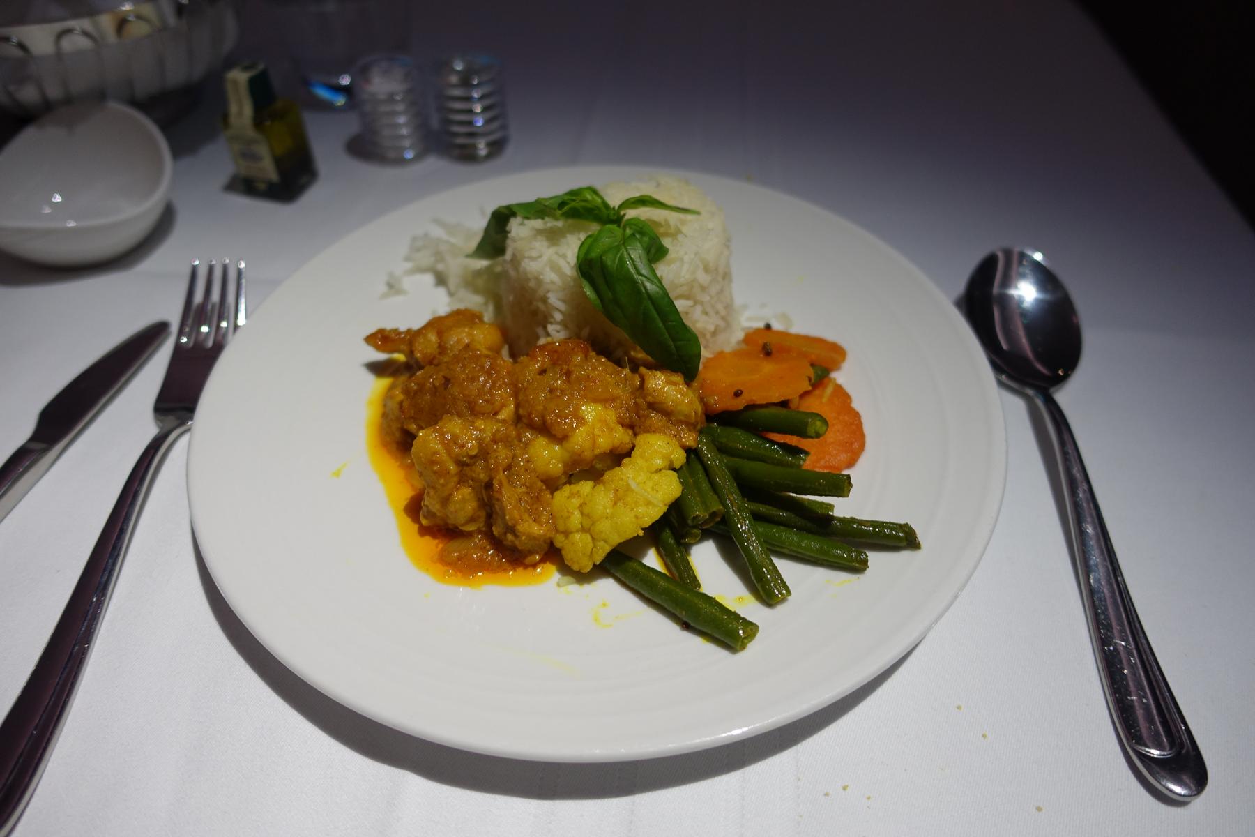 A white plate holds a first-class meal of curry, white rice, green beans, and sliced carrots.