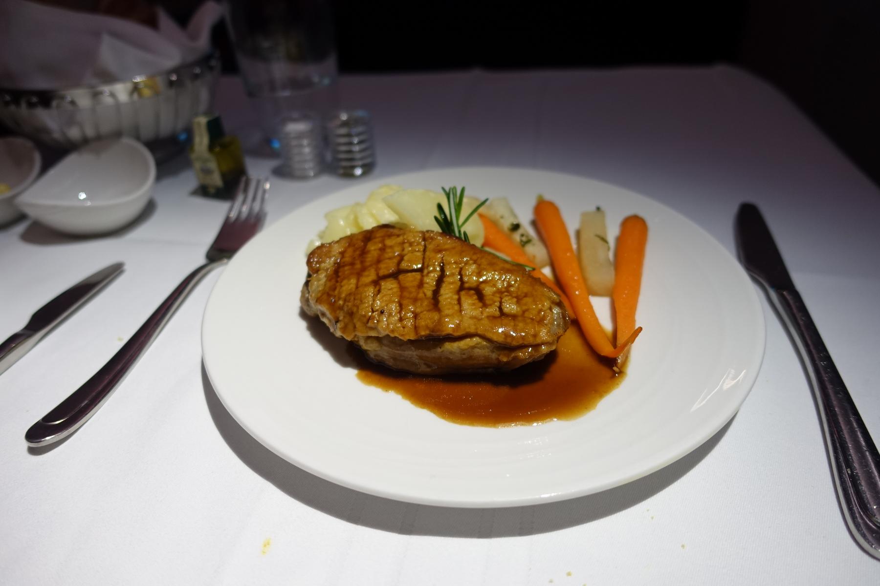 A first-class meal featuring grilled meat with a rich brown sauce, baby carrots, and potatoes on a white plate.