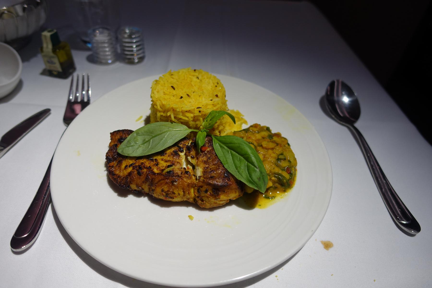 A first-class airline meal featuring grilled fish, yellow rice, and a curried side dish.