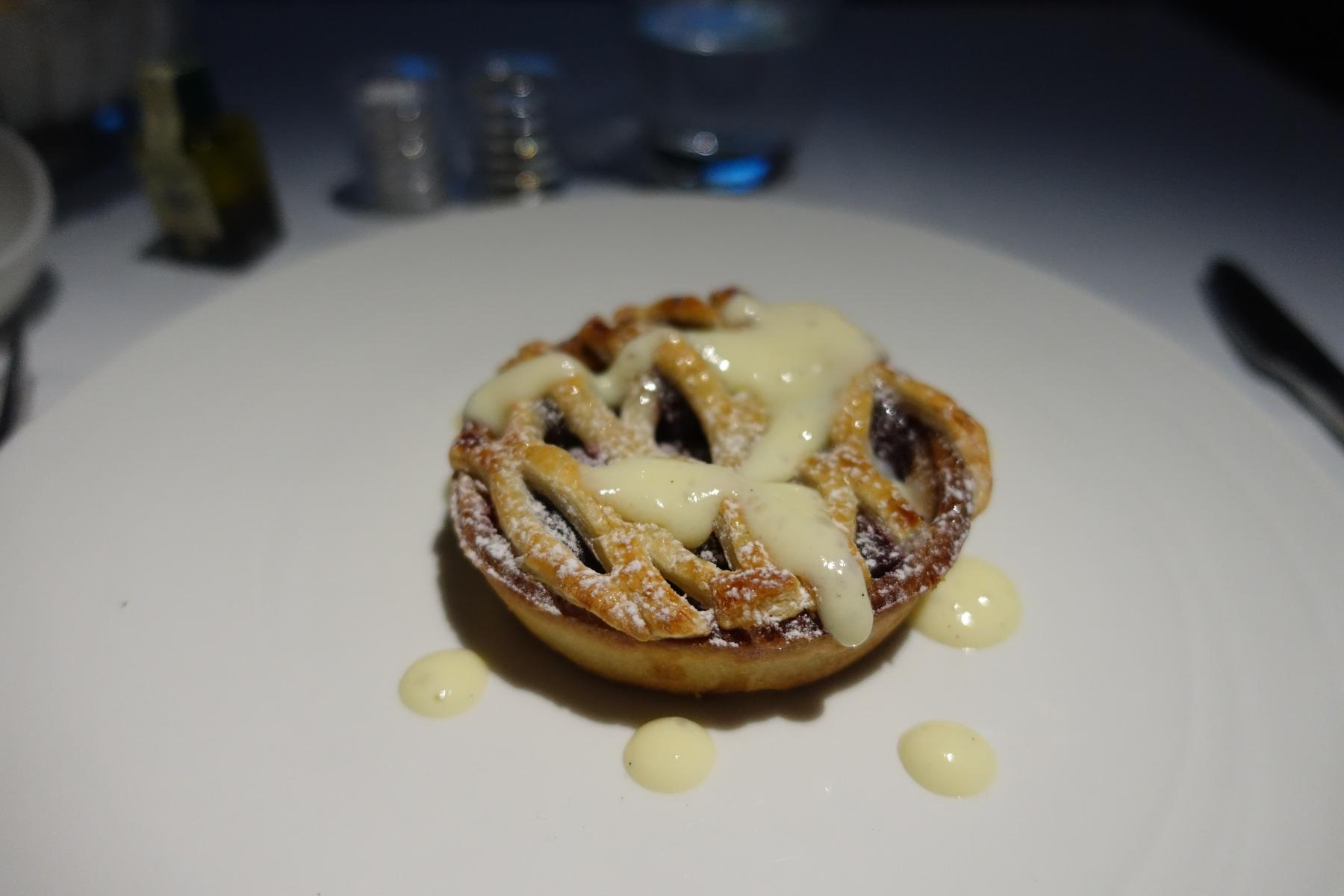 A lattice-crusted tart topped with powdered sugar and vanilla sauce on a white plate.
