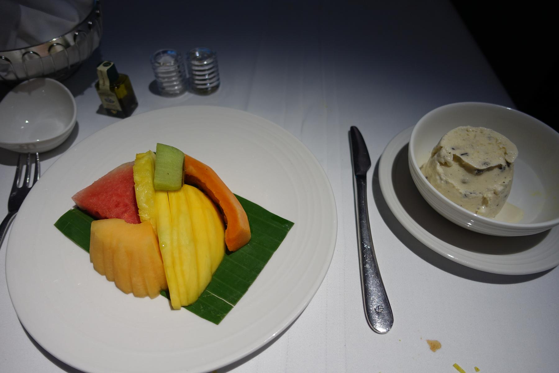A plate of sliced tropical fruit and a bowl of ice cream on a white tablecloth.