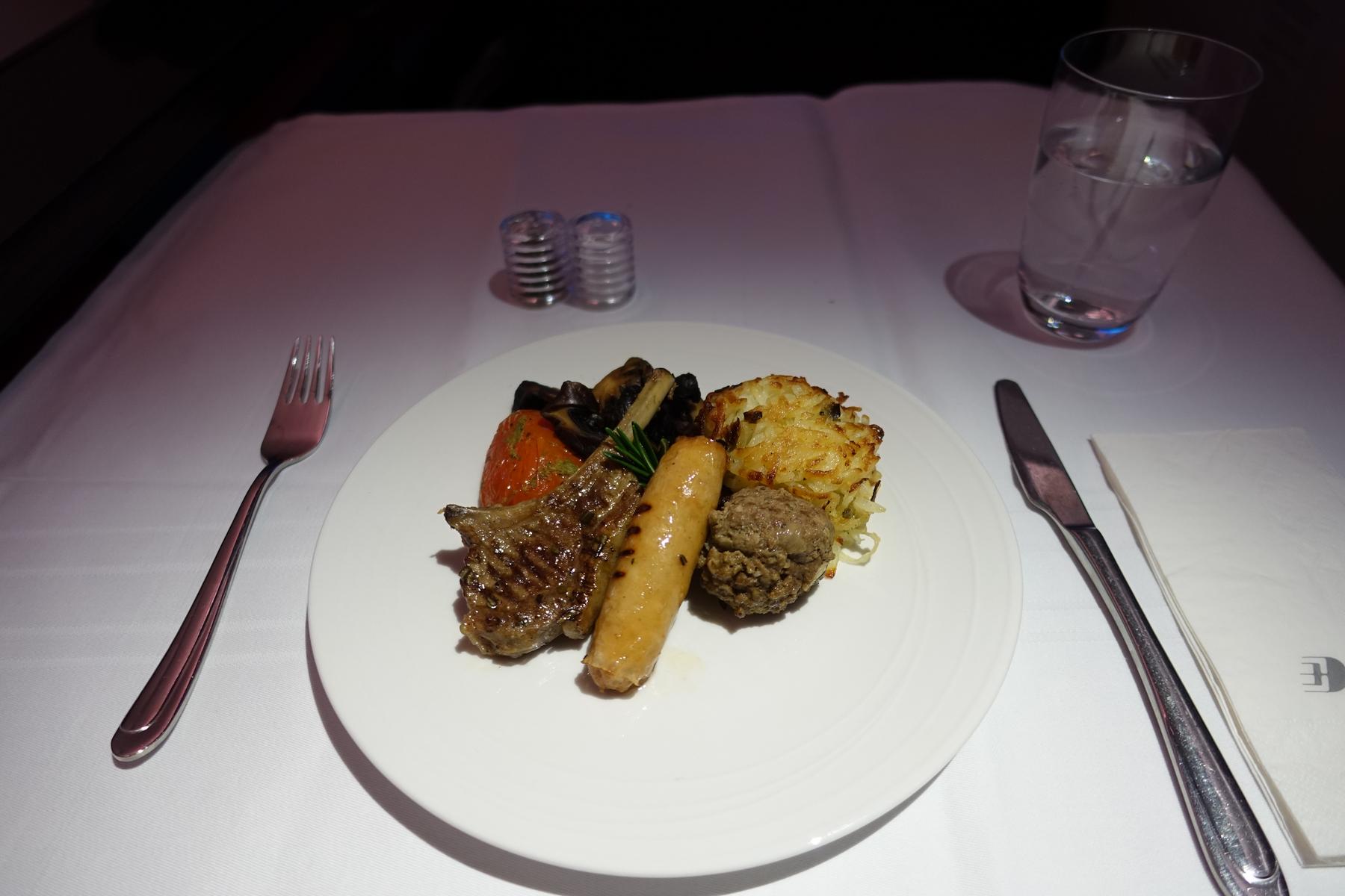 Malaysia Airlines First Class meal with lamb chop, sausage, hash brown, and roasted vegetables.