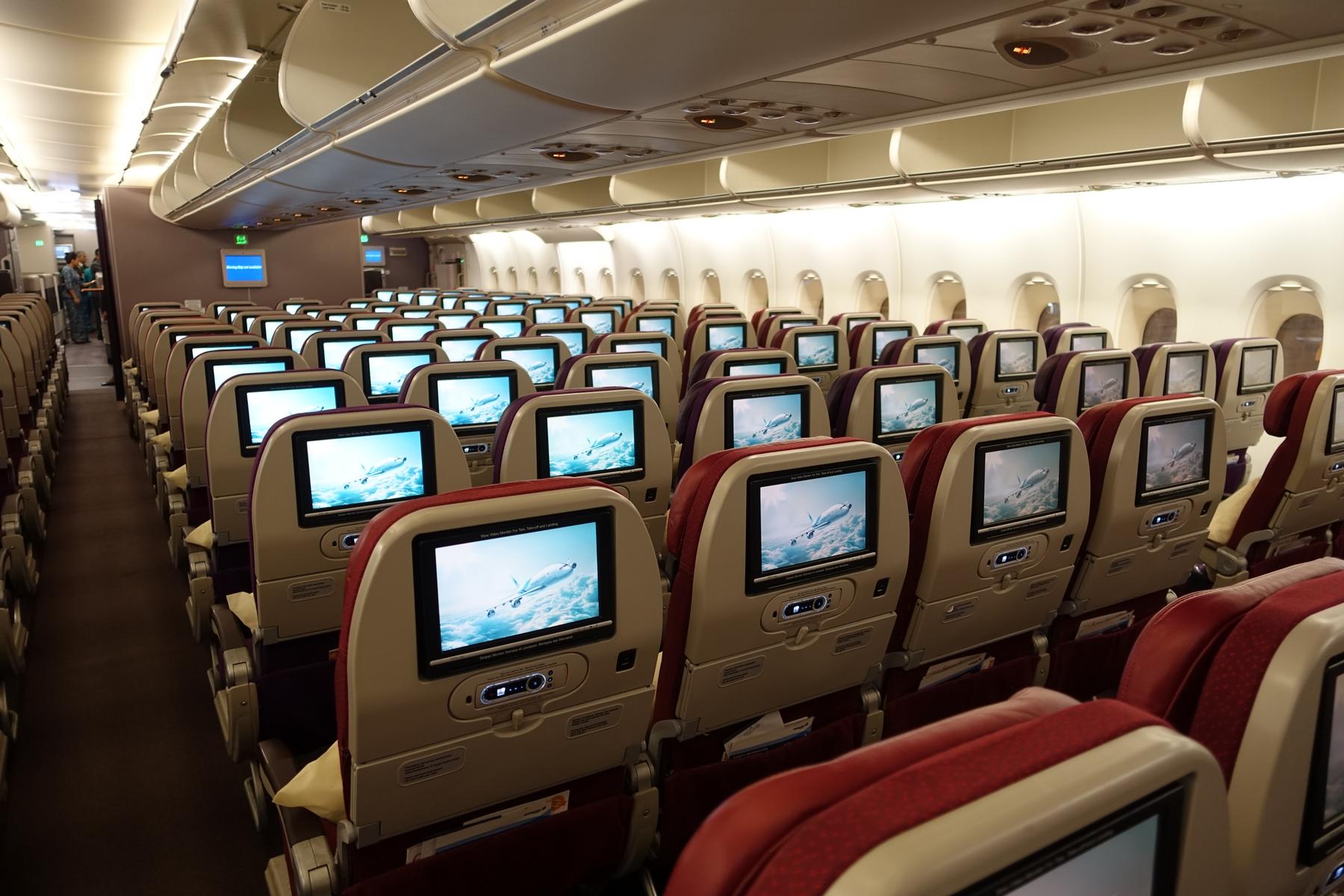Airplane cabin interior with many rows of seats, each featuring an entertainment screen displaying an airplane in flight.