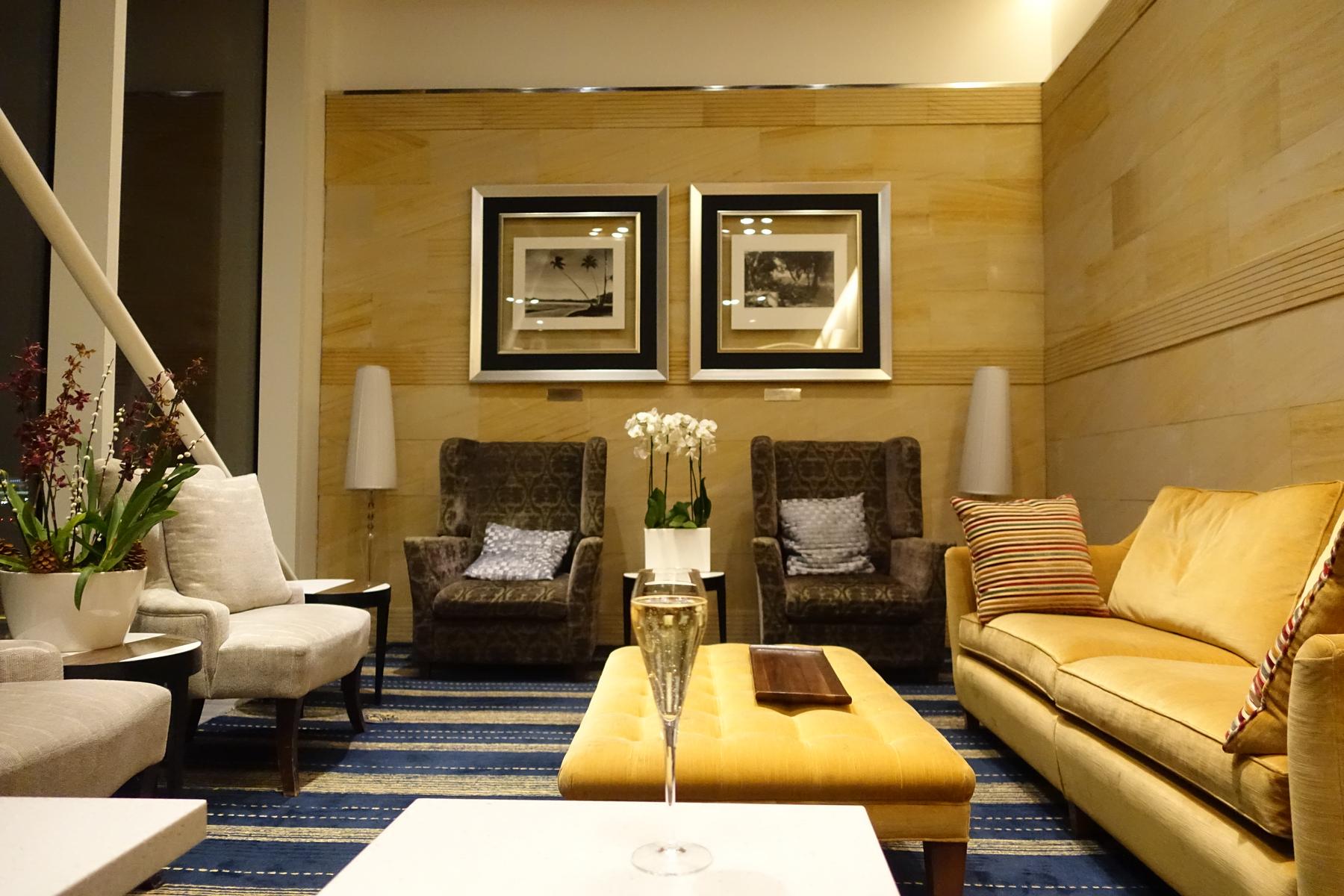 A champagne flute on a coffee table in a plush first-class airport lounge with sofas and armchairs.