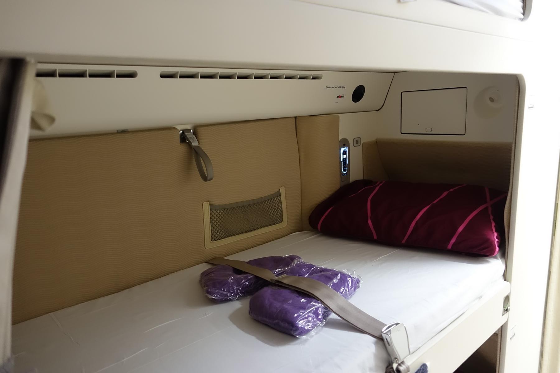 A Malaysia Airlines A380 First Class suite configured as a lie-flat bed with a pillow, amenities, and seatbelt.