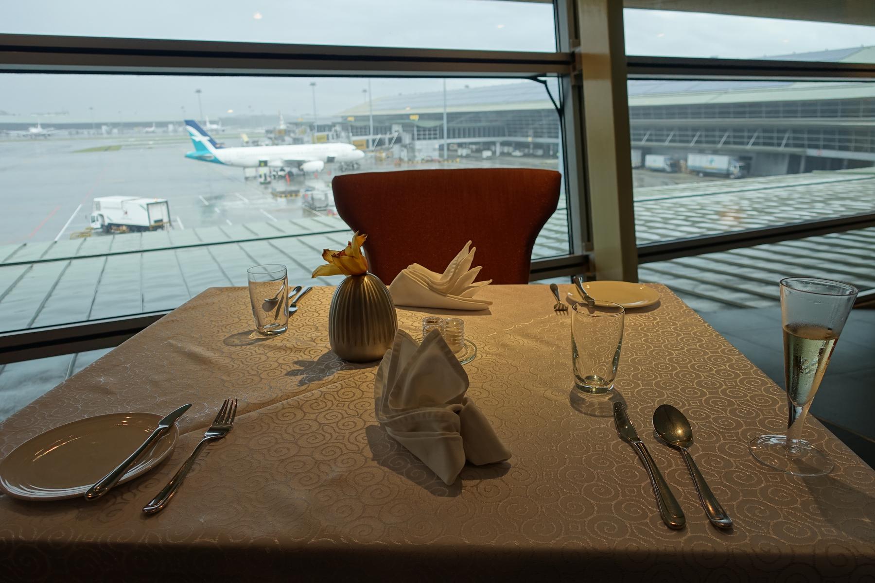 A dining table set for two in an airport lounge overlooking the tarmac with an airplane.
