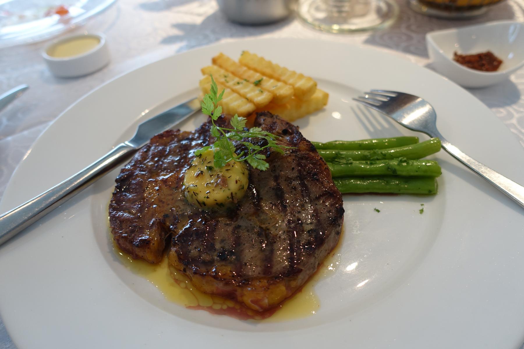 A grilled steak with butter and herbs, french fries, and green beans on a white plate.