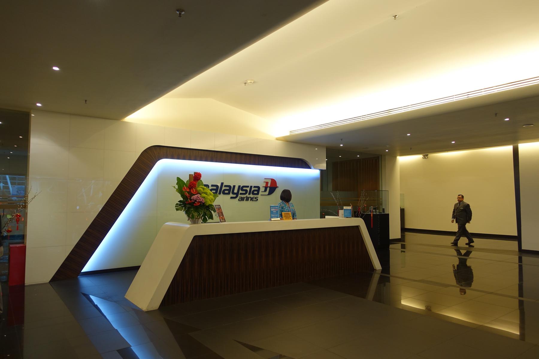 Entrance to the Malaysia Airlines First Class Lounge with a brightly lit reception desk and a man walking past.