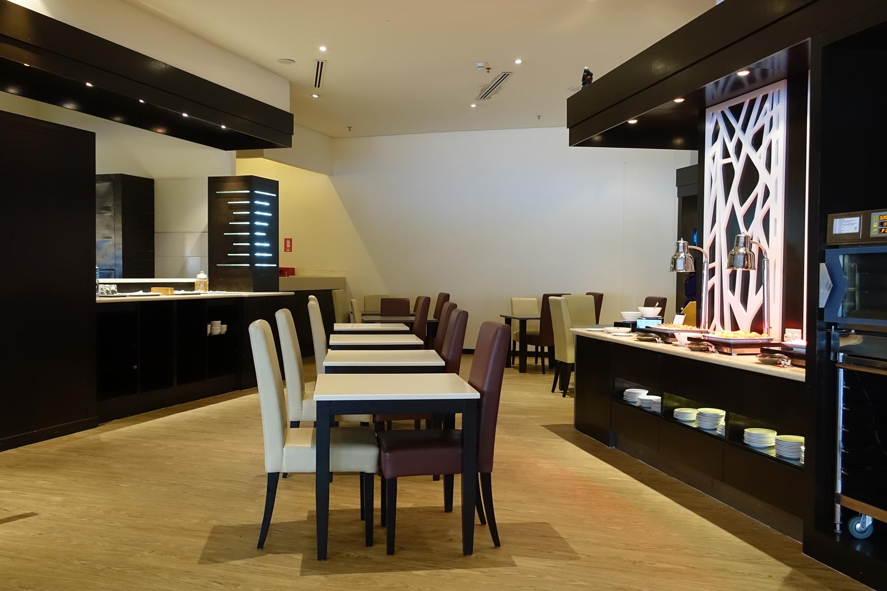 A dining area in the Malaysian Airlines First Class Lounge with tables, chairs, and a buffet.