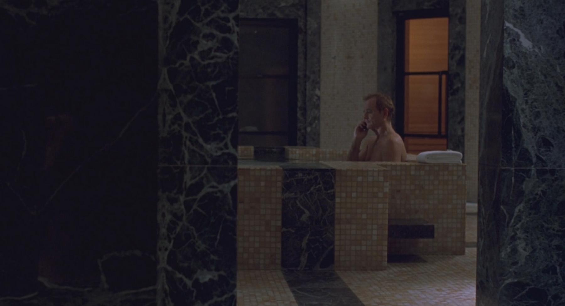 A man relaxes in a luxurious tiled bathtub while talking on a phone.