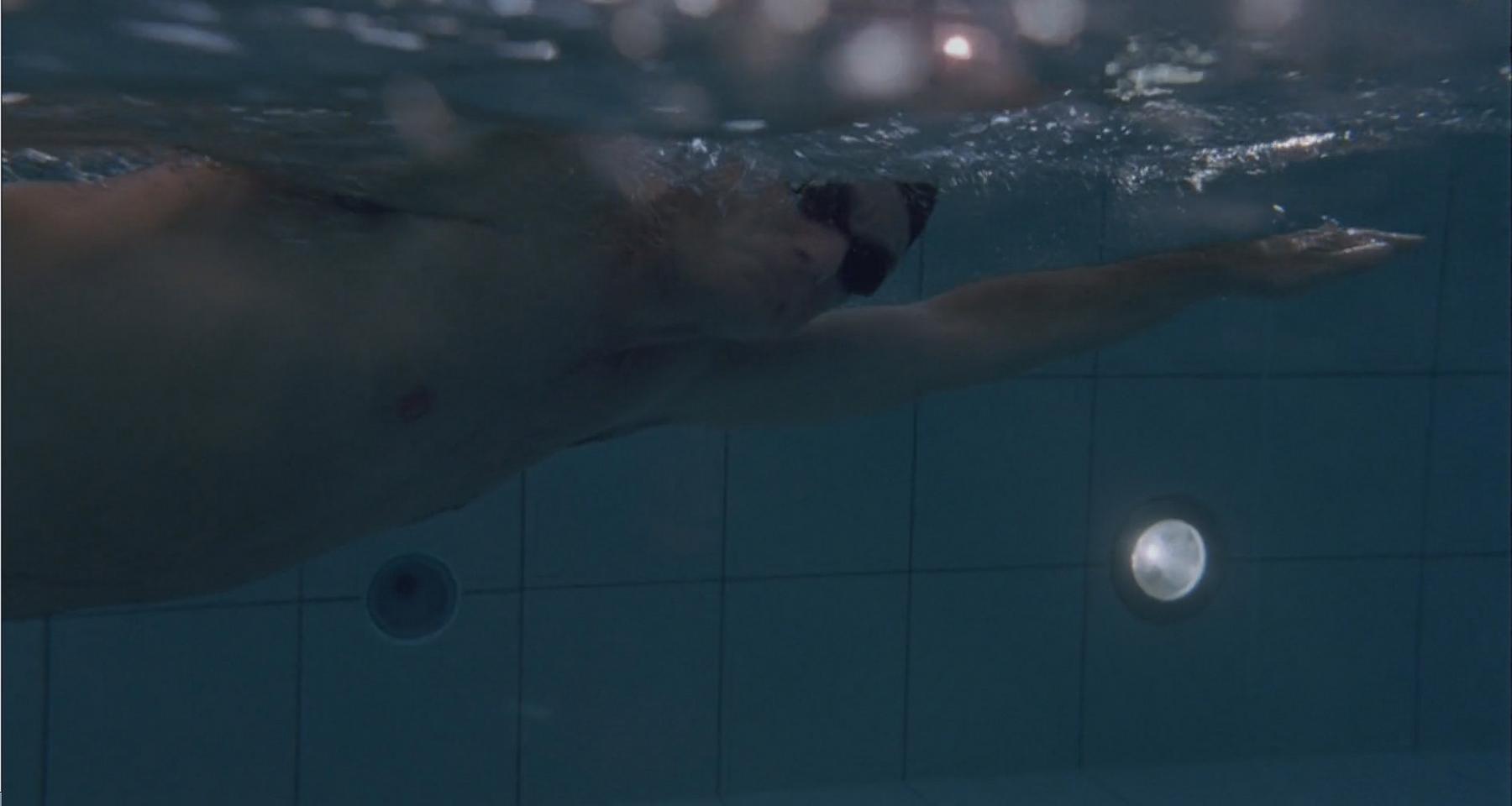 Underwater view of a person swimming with goggles in a tiled pool.