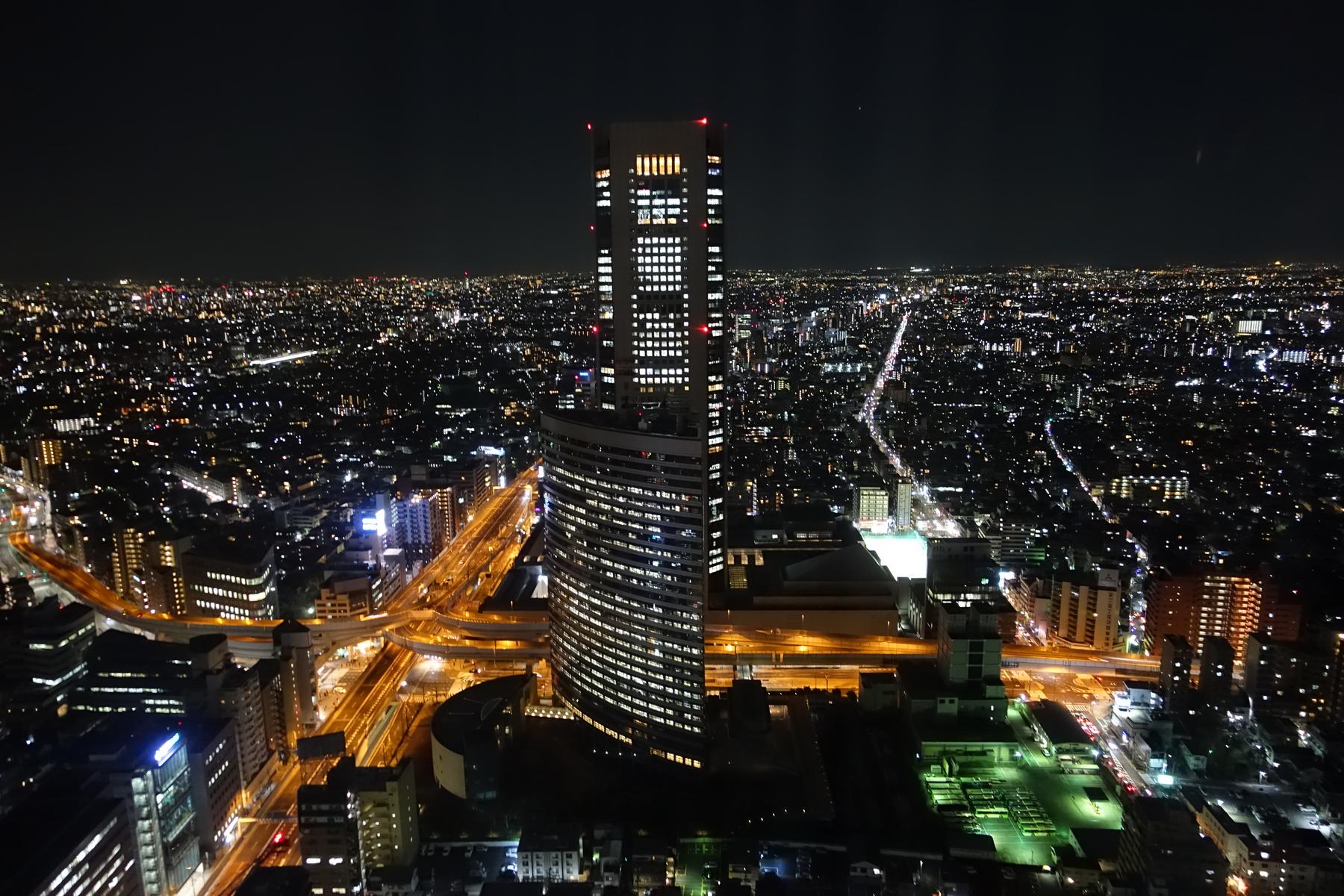 Night view of Tokyo's sprawling cityscape with a brightly lit skyscraper at its center.