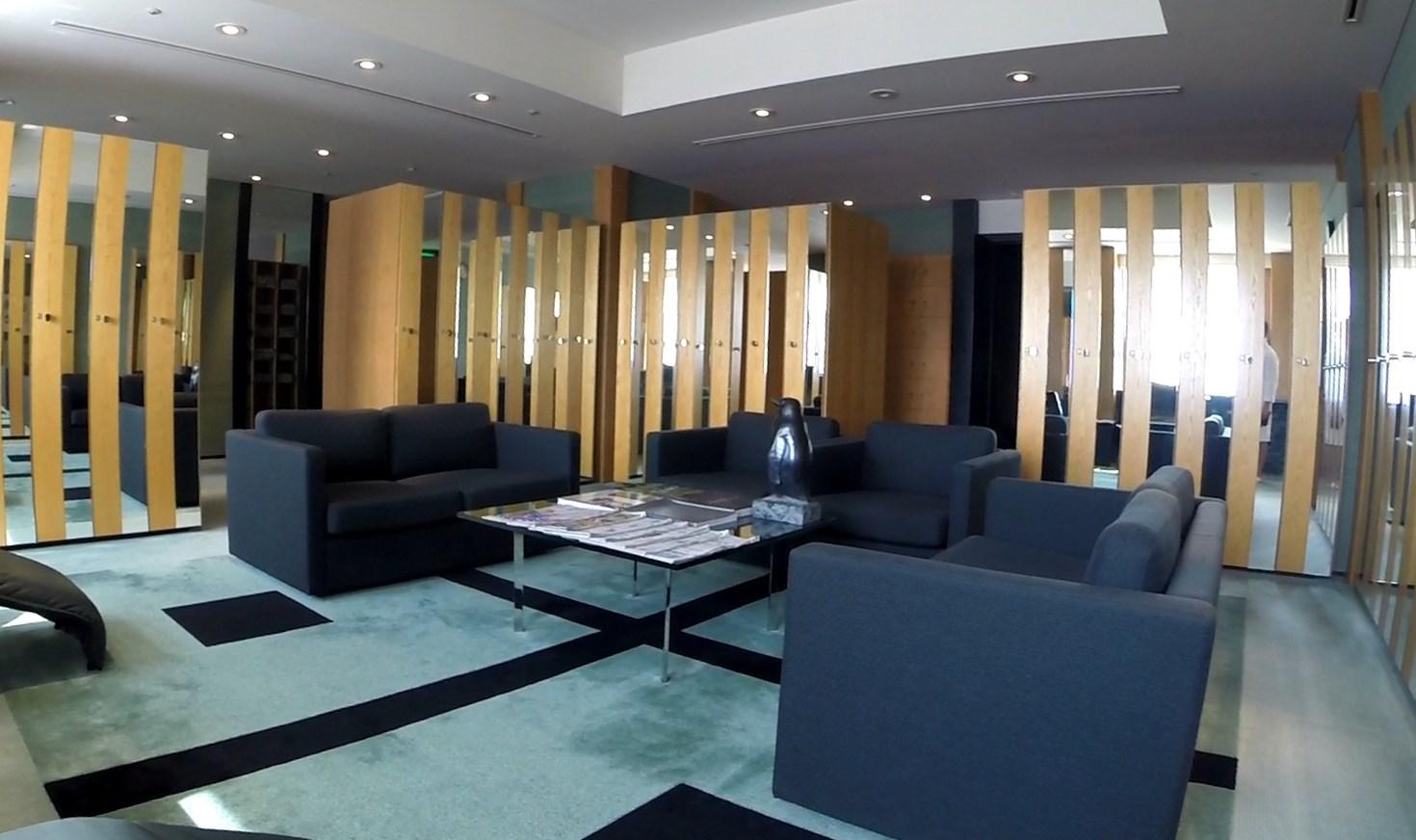 A modern hotel lounge with dark sofas, a glass coffee table holding a penguin statue, and wooden slat dividers.