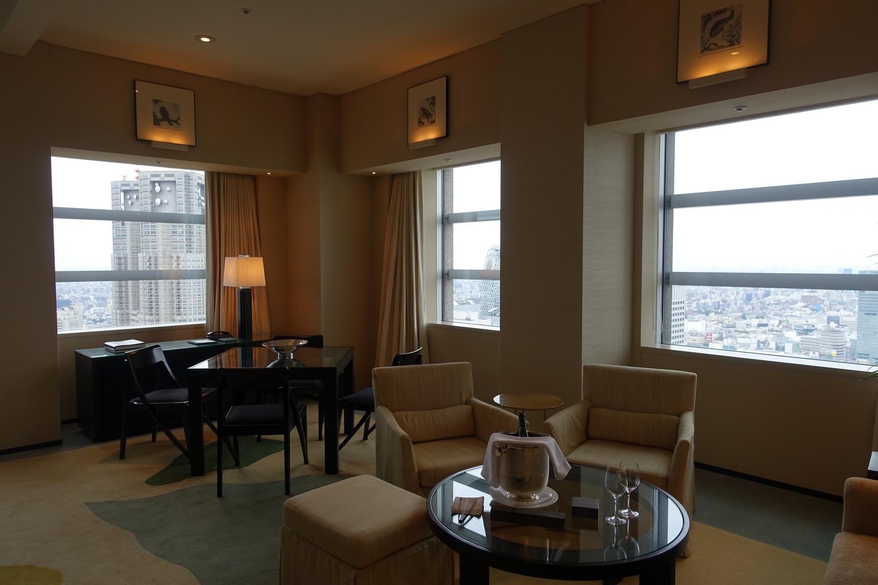 An upscale hotel suite with a city view, a dining table, and a lounge area with champagne.