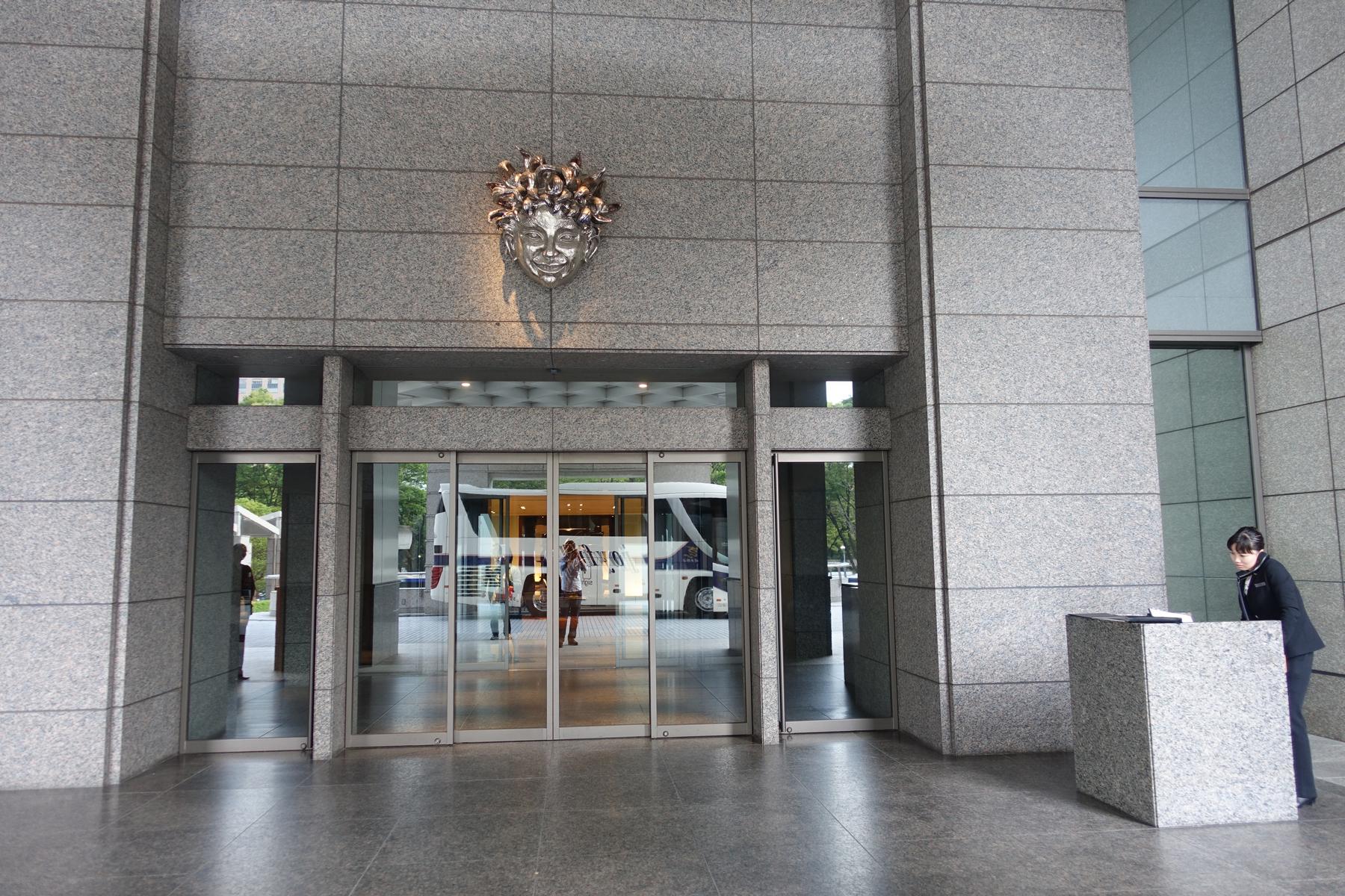 The granite entrance to the Park Hyatt Tokyo features a large metallic face sculpture above glass doors and a uniformed staff member at a desk.
