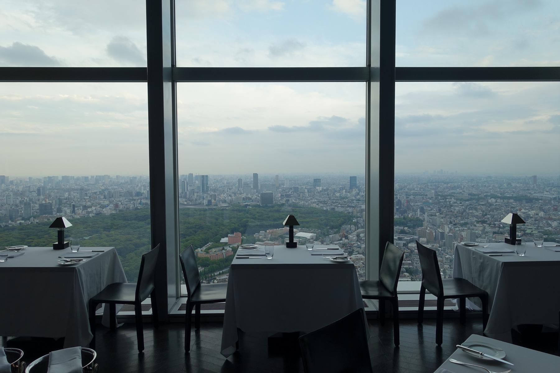 Set tables in a high-rise restaurant with panoramic views of a city and a large park.