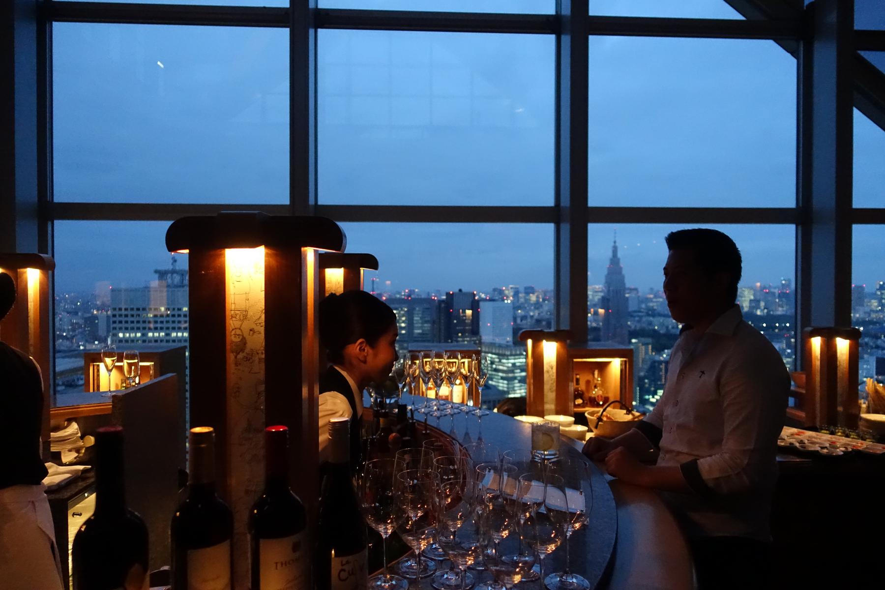 Bartender and guest at Park Hyatt Tokyo's New York Bar, with a night city skyline view.