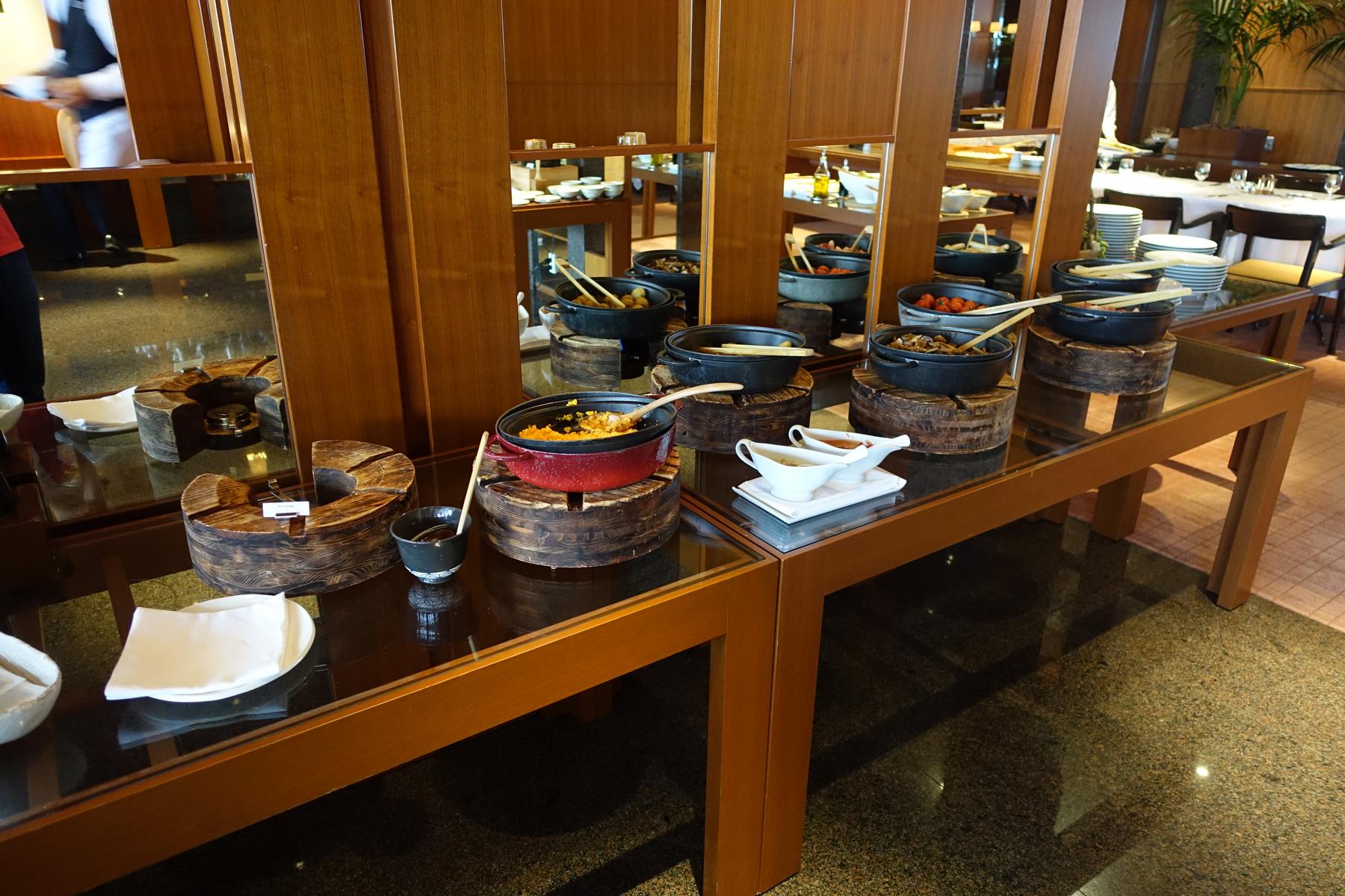 A breakfast buffet at Park Hyatt Tokyo with several hot dishes in cast iron pots on a long glass table.