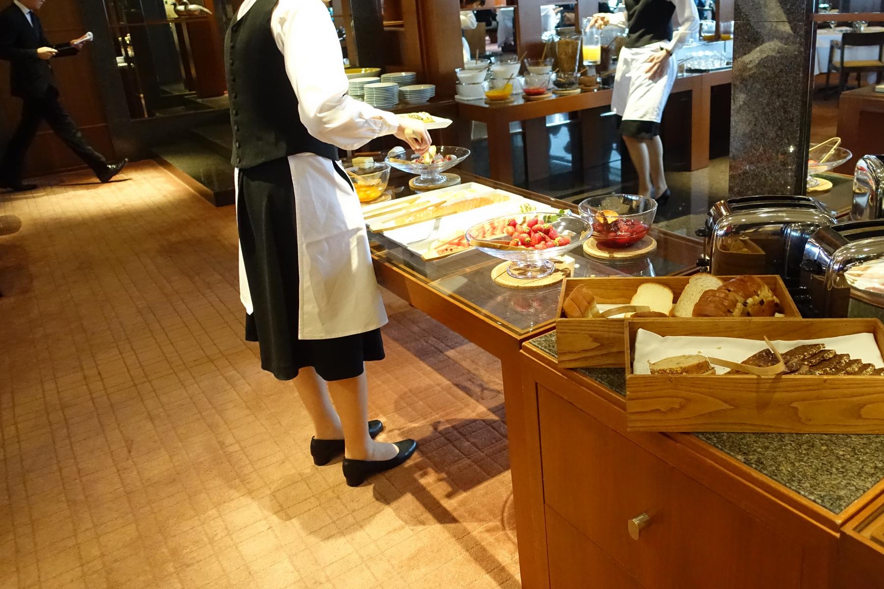 A server tends to a breakfast buffet featuring fresh fruit, pastries, and bread.
