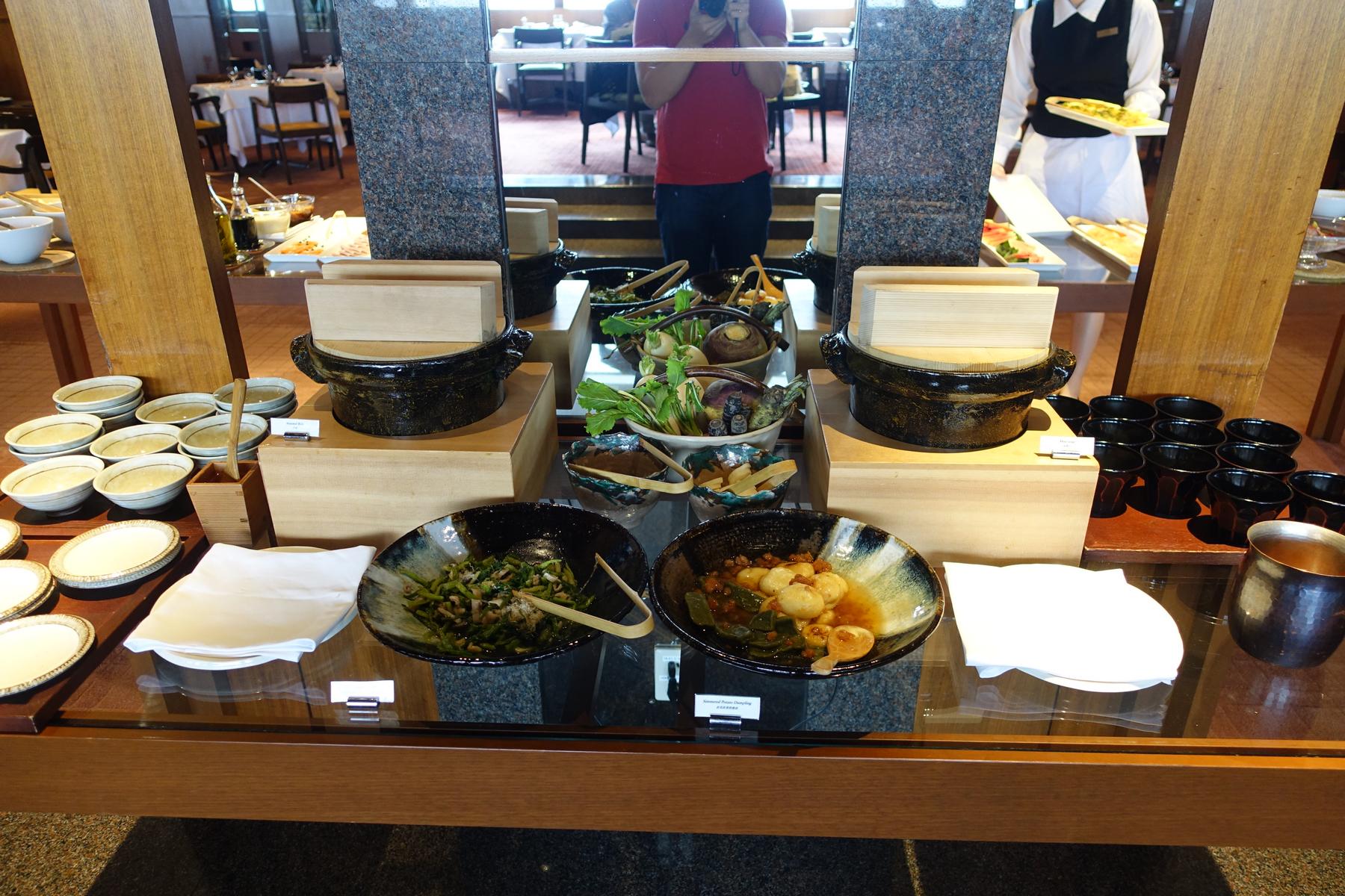 A Japanese-style breakfast buffet featuring steamed dishes, prepared vegetables, and small serving bowls.