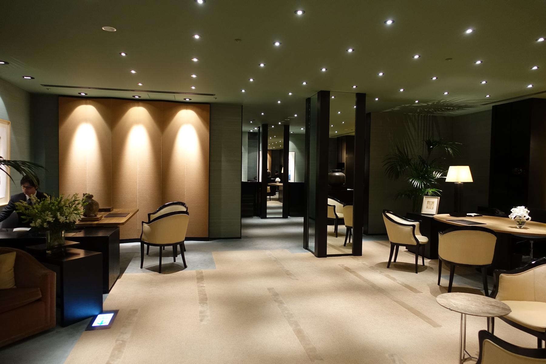 An elegant, modern hotel lobby with a reception desk, beige armchairs, and warm accent lighting.