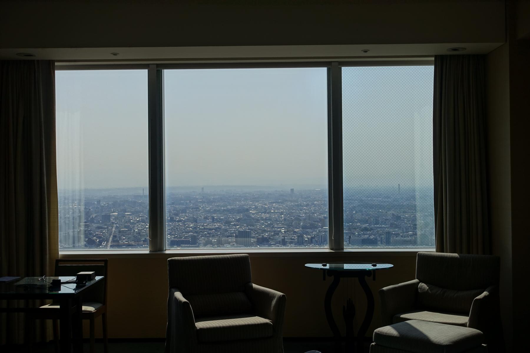 A room with two armchairs facing large windows that offer an expansive city view.