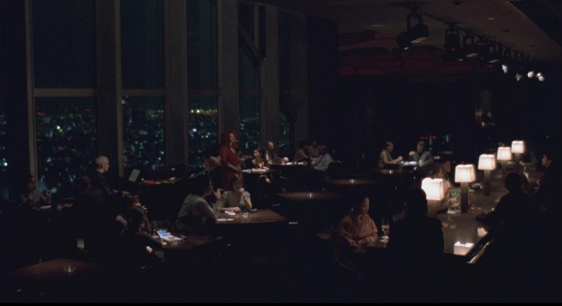 The dimly lit New York Bar at night, with patrons, a singer, and a city skyline through large windows.