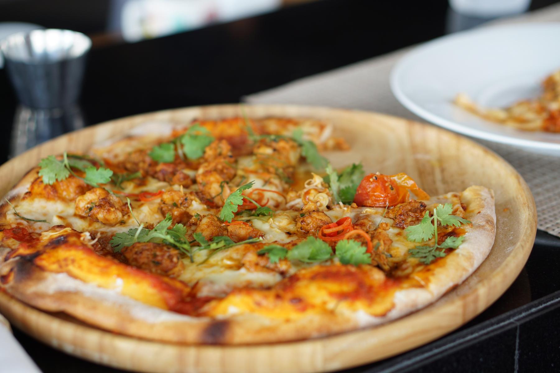 A shrimp pizza topped with cilantro and chili, served on a wooden platter.