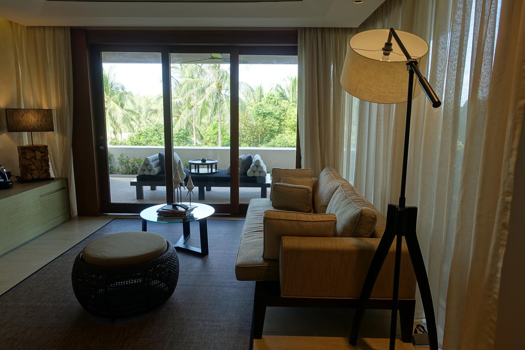 A modern hotel suite living area with a balcony overlooking tropical palm trees.