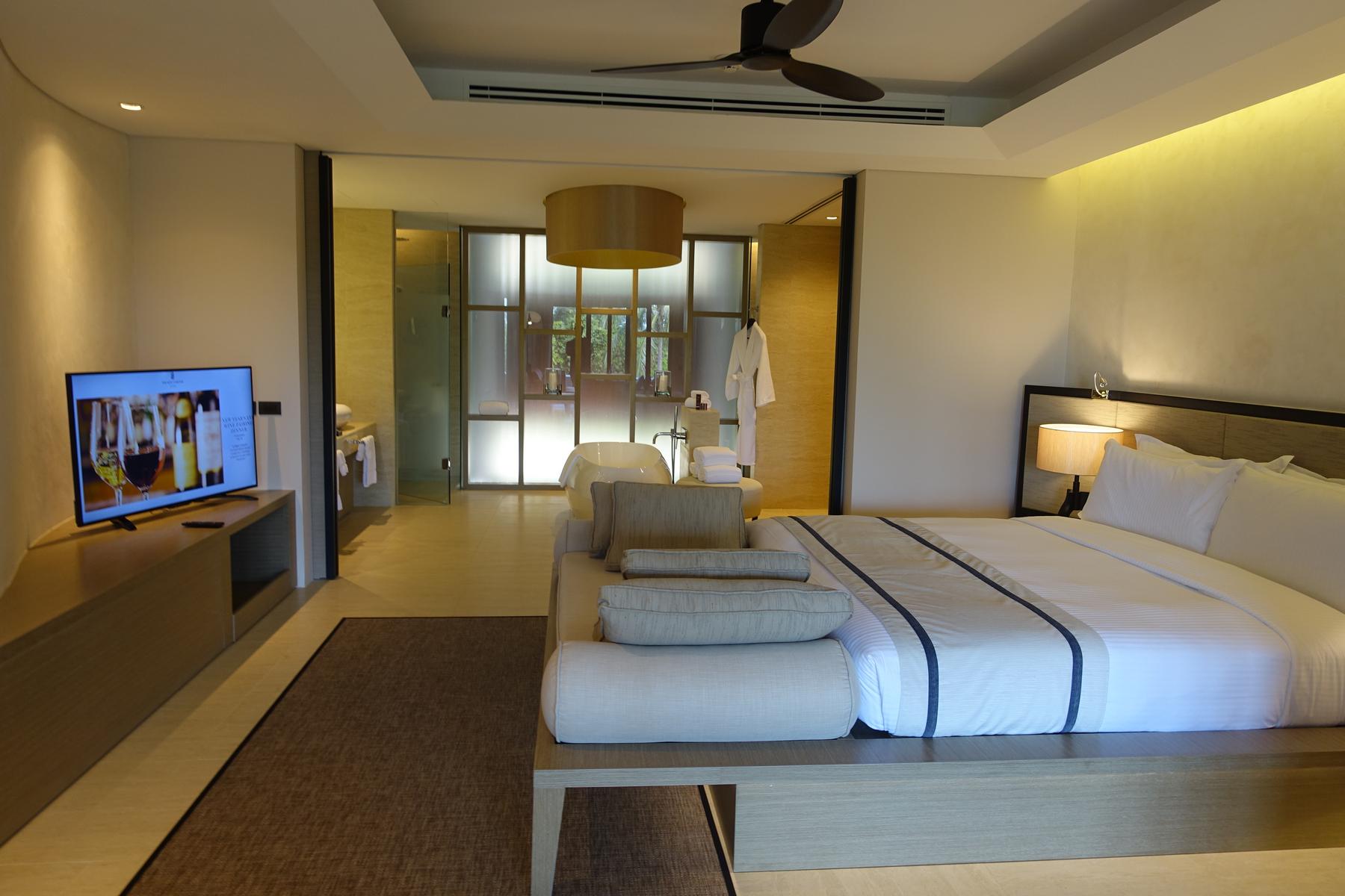 A spacious, modern hotel room with a large bed, television, and an open-concept bathroom featuring a freestanding tub.