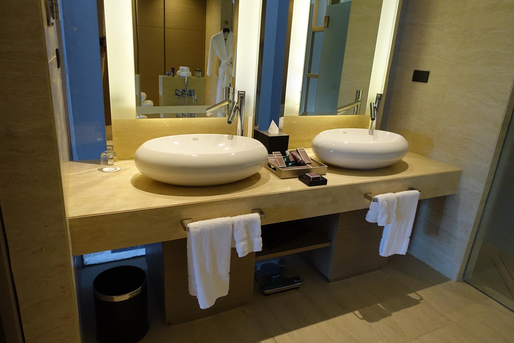 Two sleek white vessel sinks on a light marble vanity in a modern hotel bathroom.
