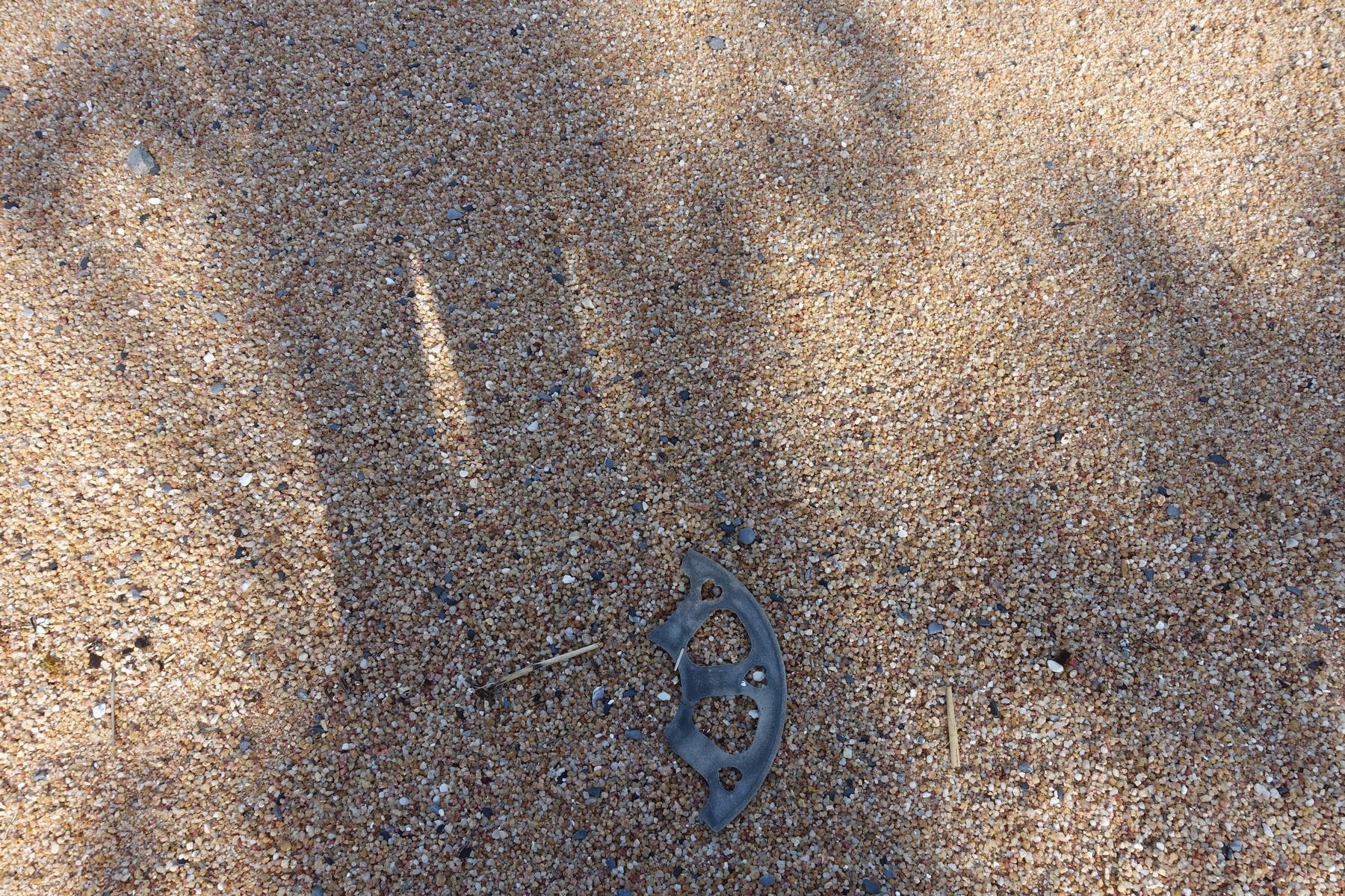 Broken dark plastic debris on coarse sand.
