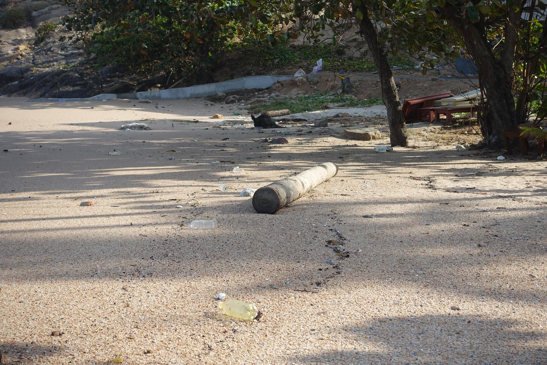 A sandy beach littered with plastic bottles and a large log.