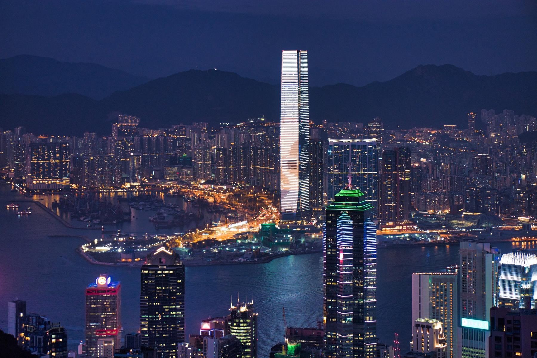 Night view of Hong Kong's illuminated skyline with prominent skyscrapers and a harbor.