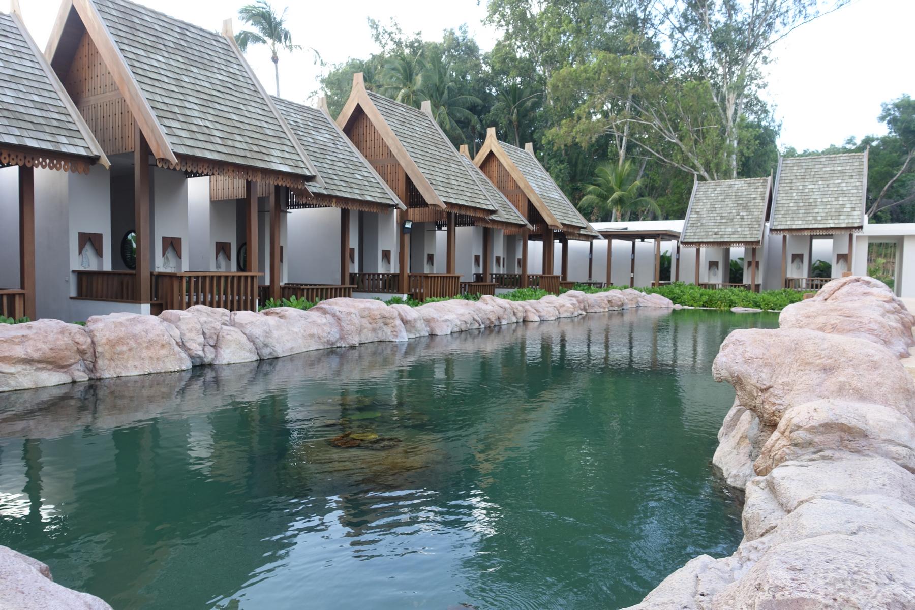 Traditional Thai-style villas with peaked wooden roofs overlook a tranquil resort pond.
