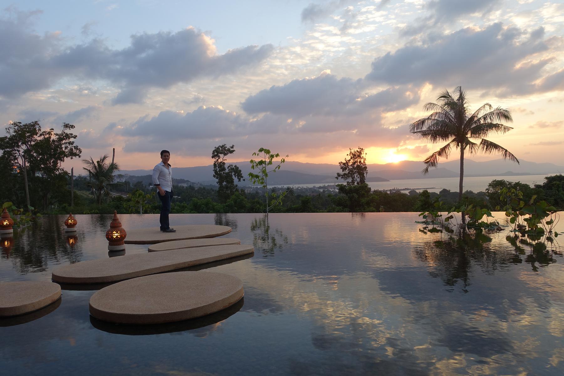 Man standing on stepping stones in an infinity pool at sunset in Koh Samui.