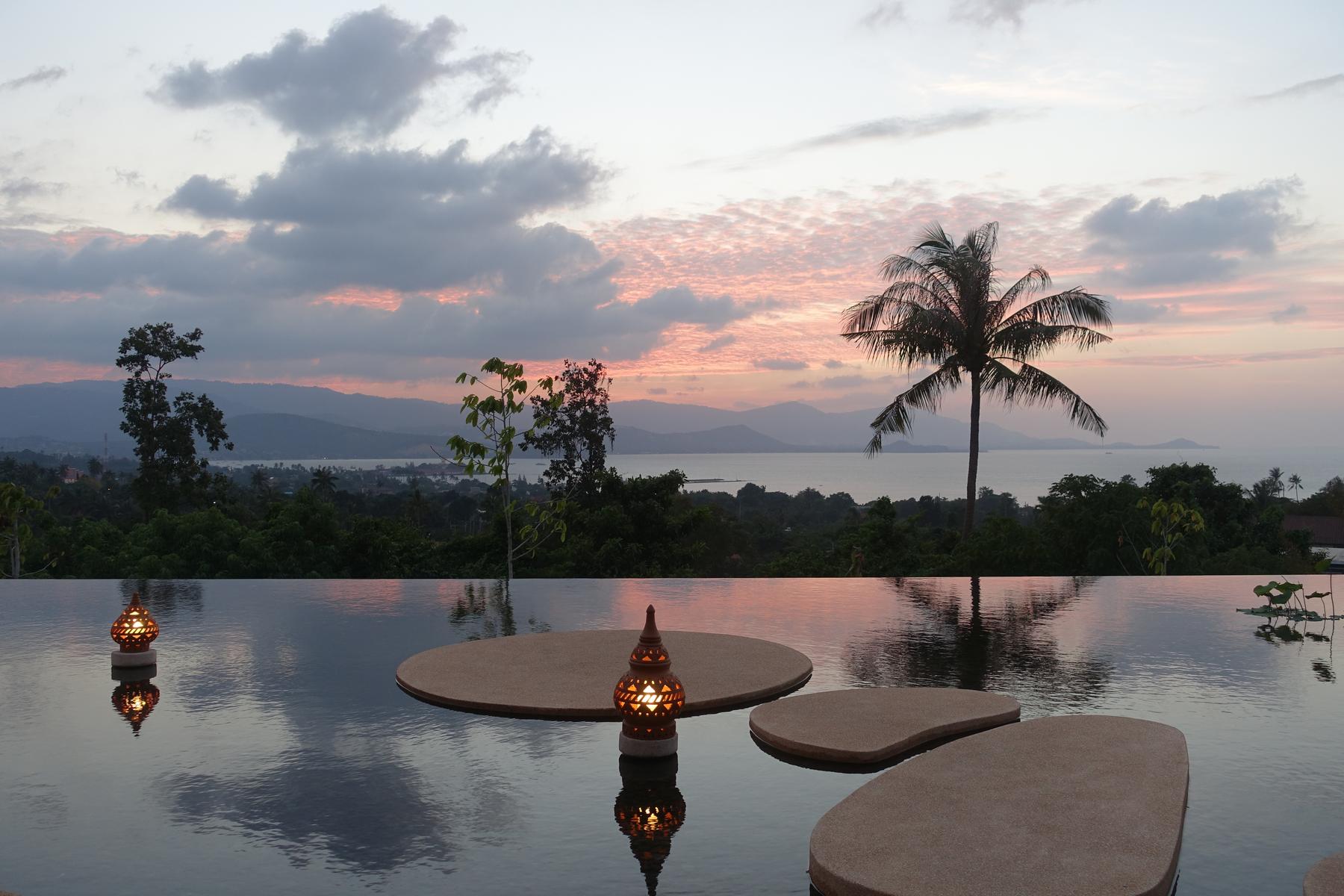 Infinity pool with glowing lanterns and floating platforms overlooking a tropical bay and sunset.