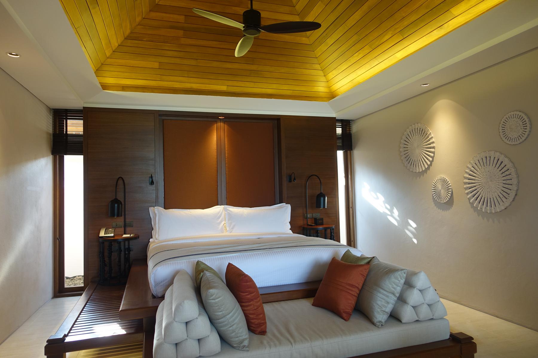 A luxurious hotel room at the Ritz Carlton Koh Samui, featuring a large bed, a wooden vaulted ceiling, and a daybed.