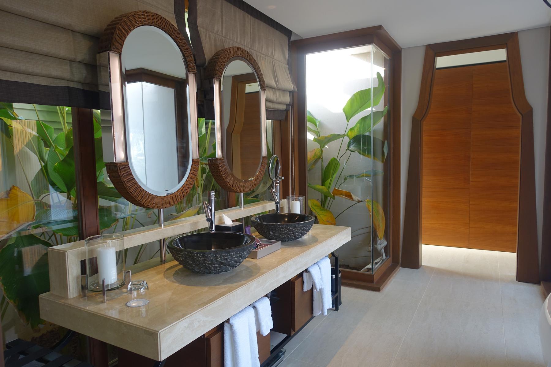 A well-appointed bathroom with a double vanity, dark vessel sinks, and large windows revealing tropical foliage.