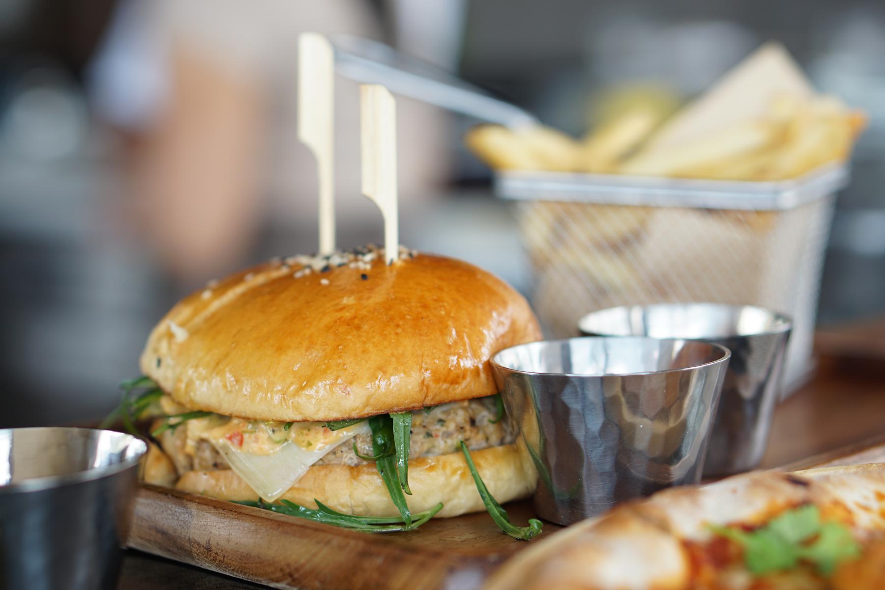 A gourmet burger, fries, and two sauce cups served on a wooden board.