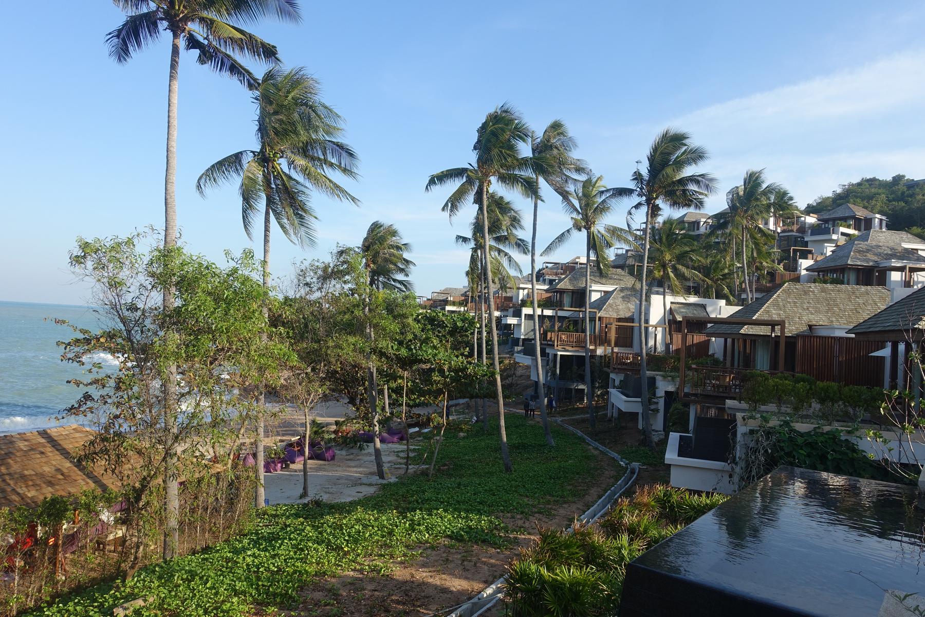 Ritz Carlton Koh Samui resort with hillside villas, palm trees, and ocean.