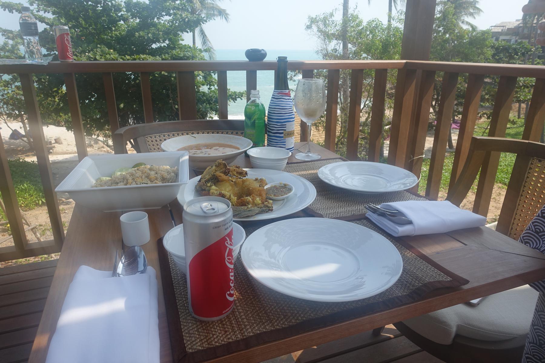 A balcony table set with fried fish, rice, and drinks, overlooking the ocean.