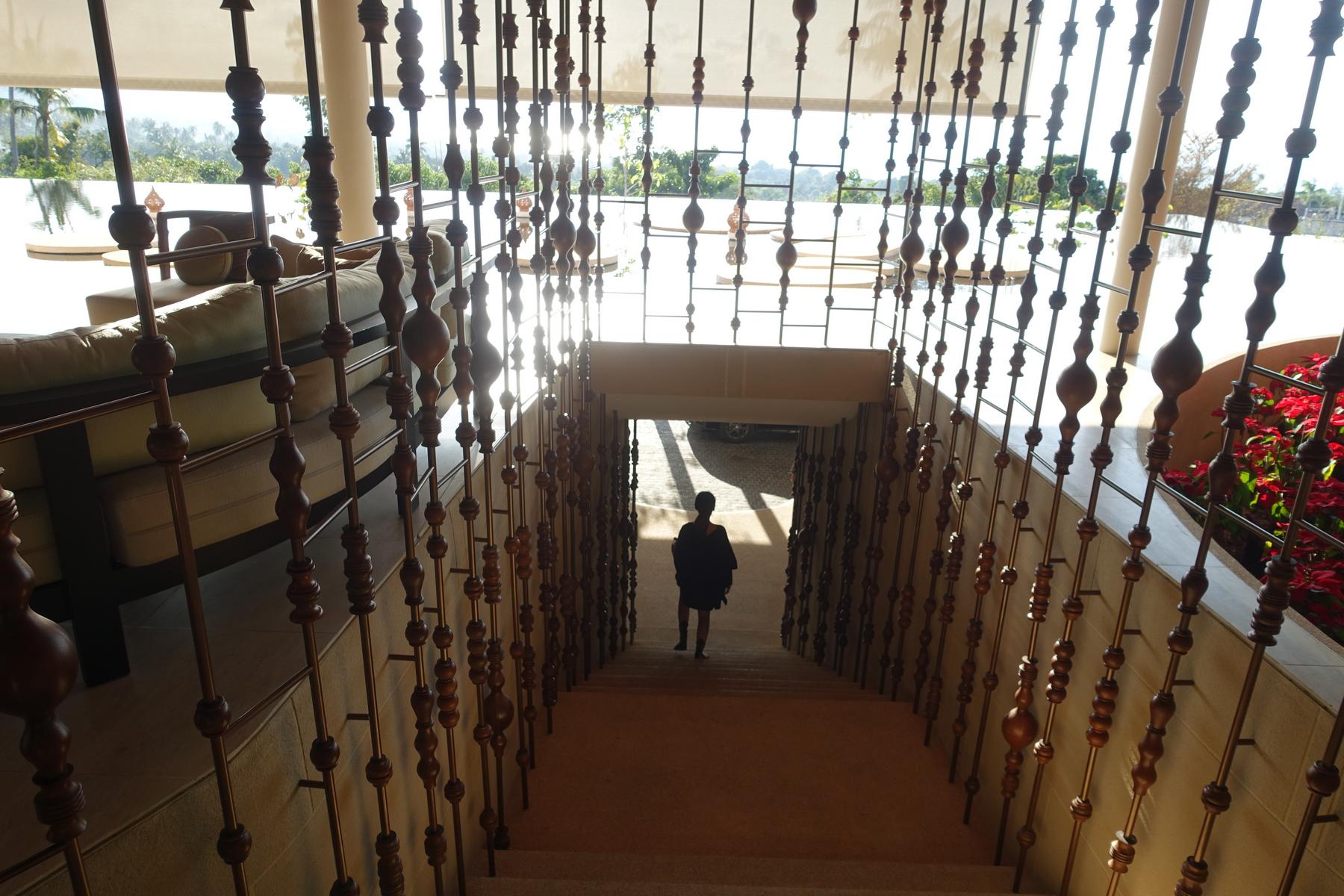 A person walks down an ornate staircase, silhouetted against bright sunlight.
