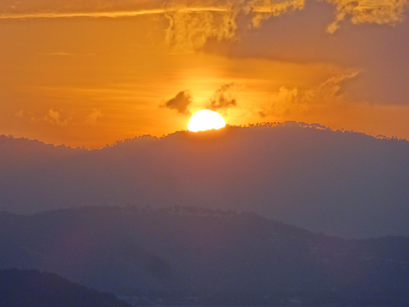 A bright orange sun peeking over hazy mountains at sunset.