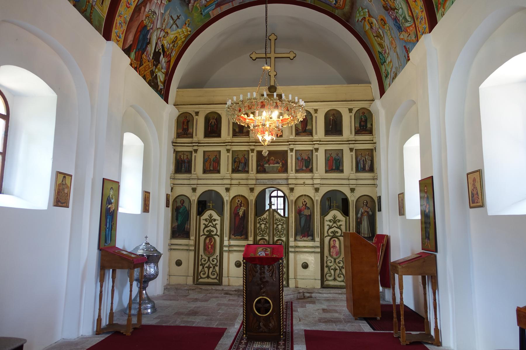 Interior view of an Orthodox church with a large iconostasis, ornate chandelier, and colorful ceiling frescoes.