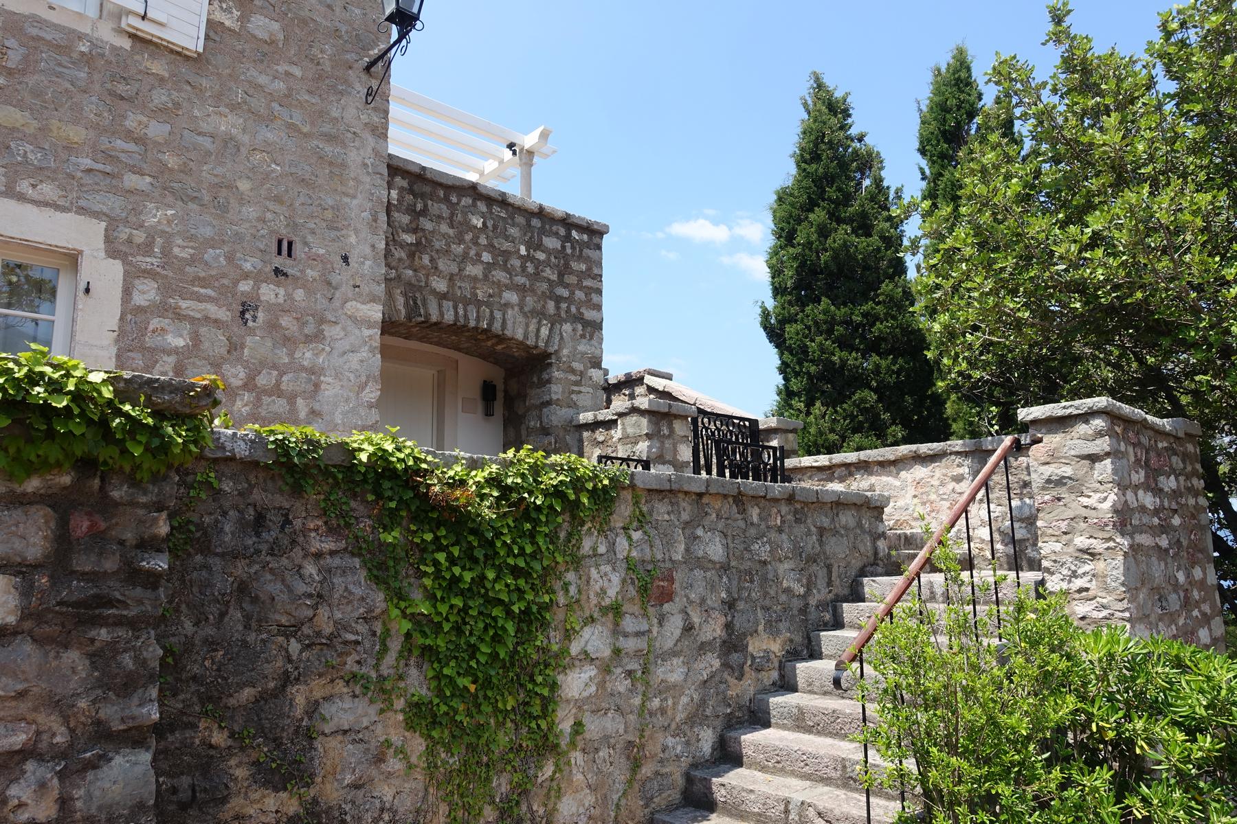 A stone building with an arched entrance and a stone staircase, surrounded by ivy-covered walls and trees.