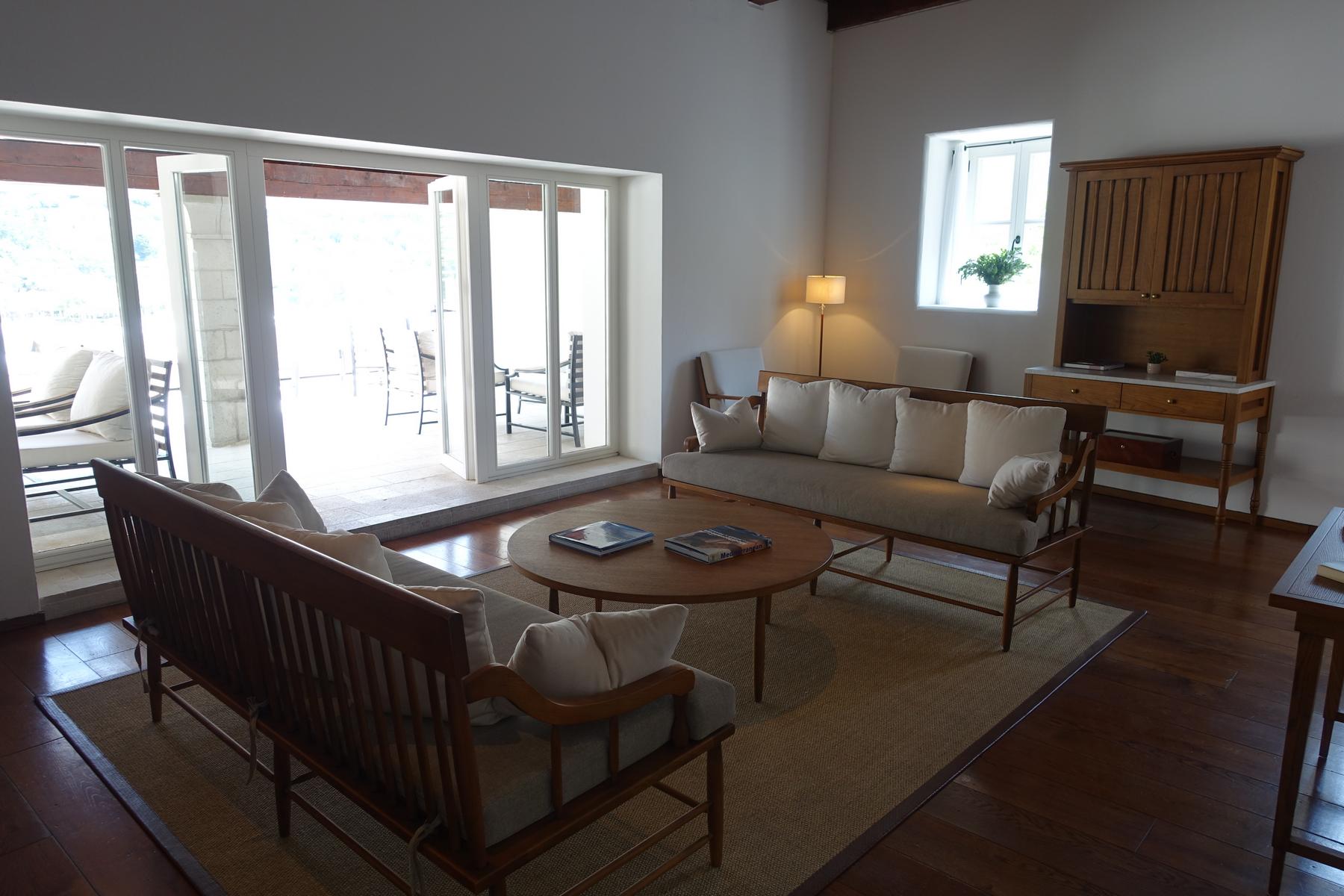 A bright, luxurious living room with light wooden furniture, a woven rug, and glass doors opening to an outdoor patio.