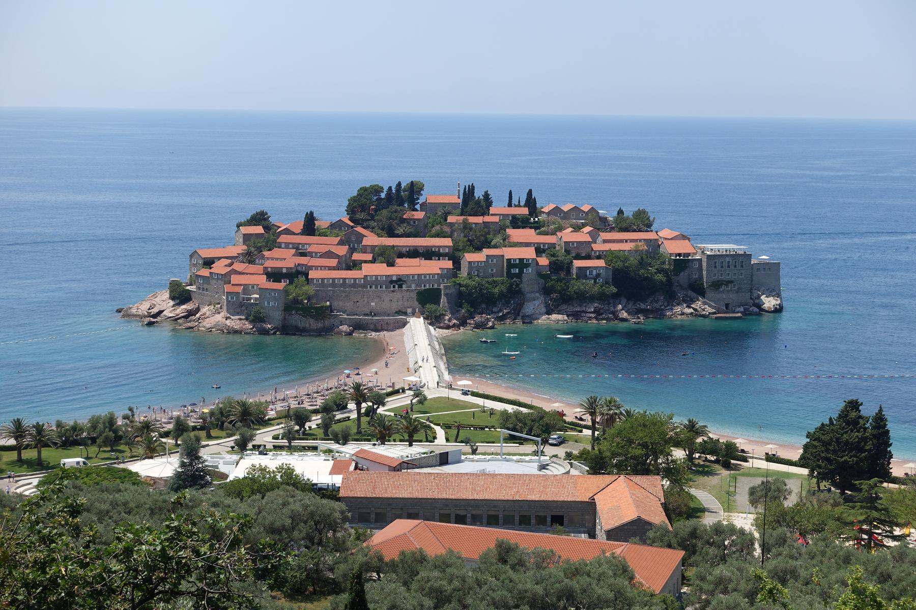 Sveti Stefan Islet, a historic village with red-roofed buildings, connected to the mainland by a causeway with beaches.