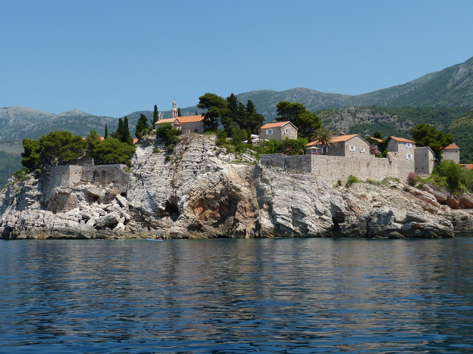 Sveti Stefan islet, a rocky island village with red-roofed stone buildings, viewed from the sea.