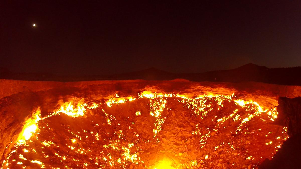 Darvaza Gas Crater blazing with fire at night under a moonlit sky.